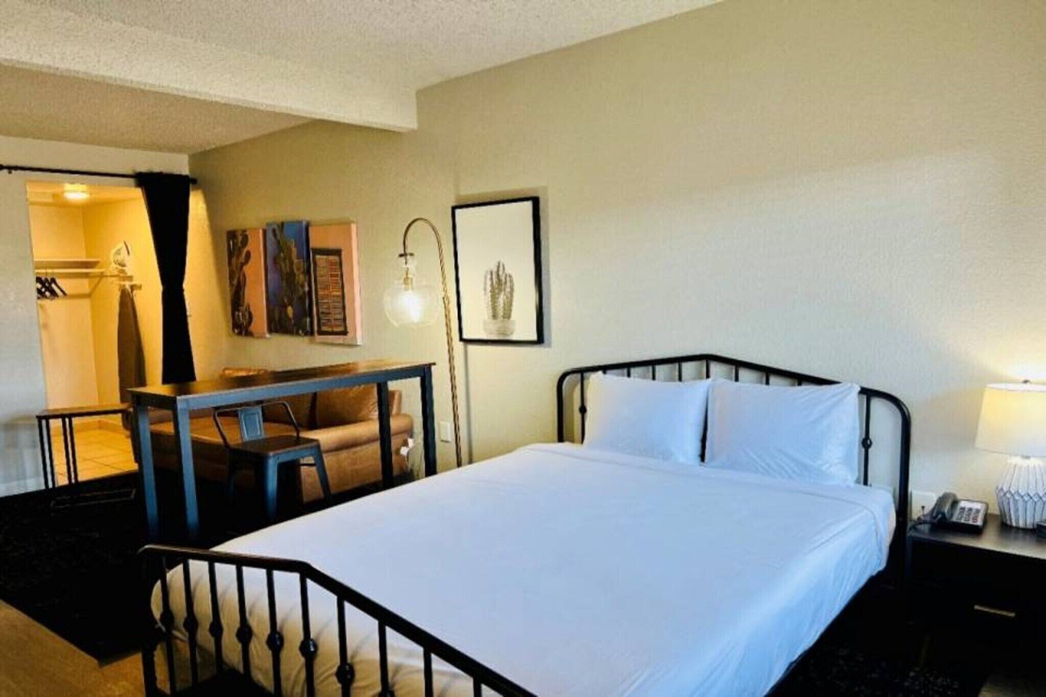 Habitación de hotel con cama, escritorio, silla, lámpara y un cuadro en la pared.