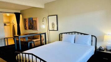 Habitación de hotel con cama, escritorio, silla, lámpara y un cuadro en la pared.