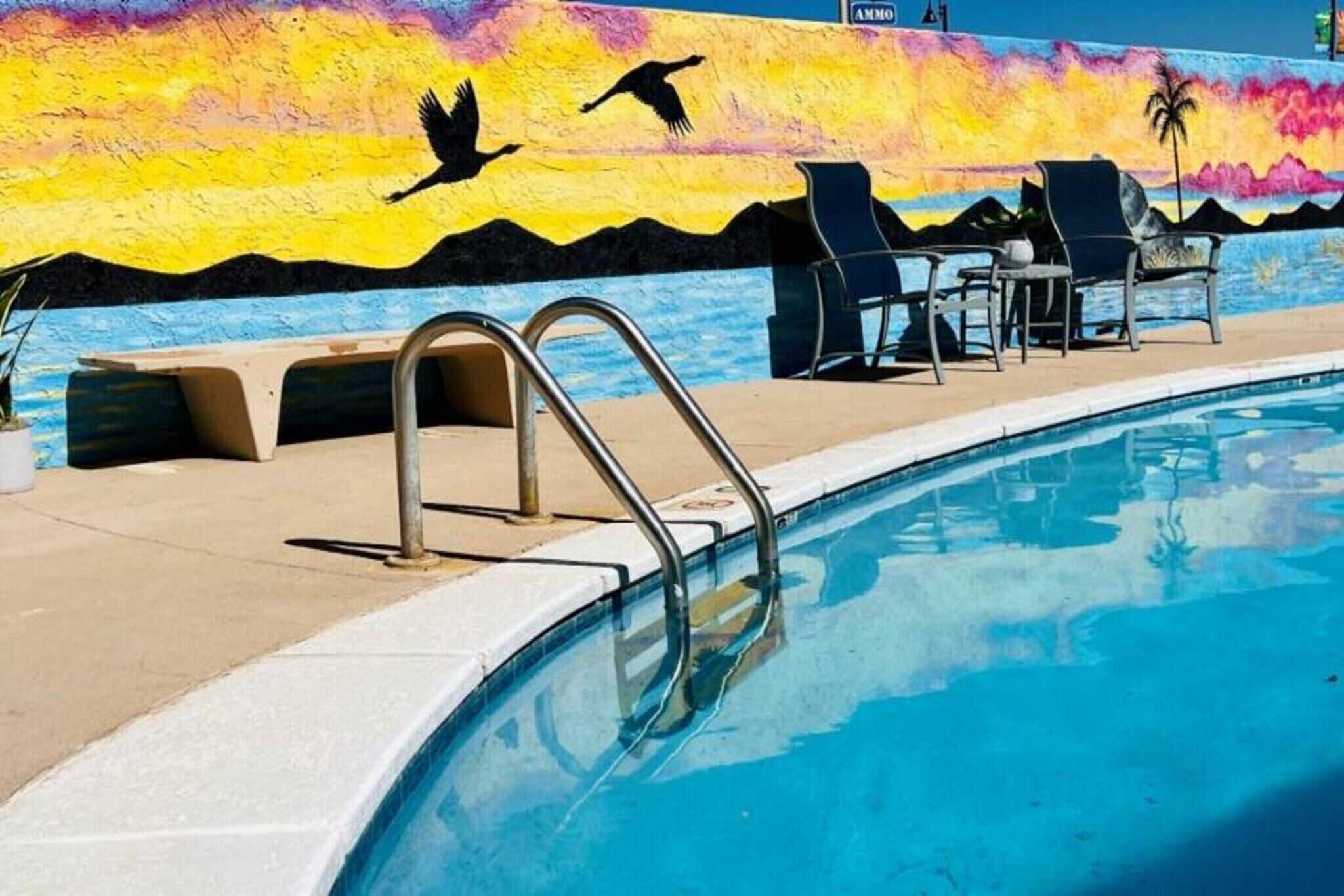 En swimmingpool med en väggmålning, solstolar och en metallstege.