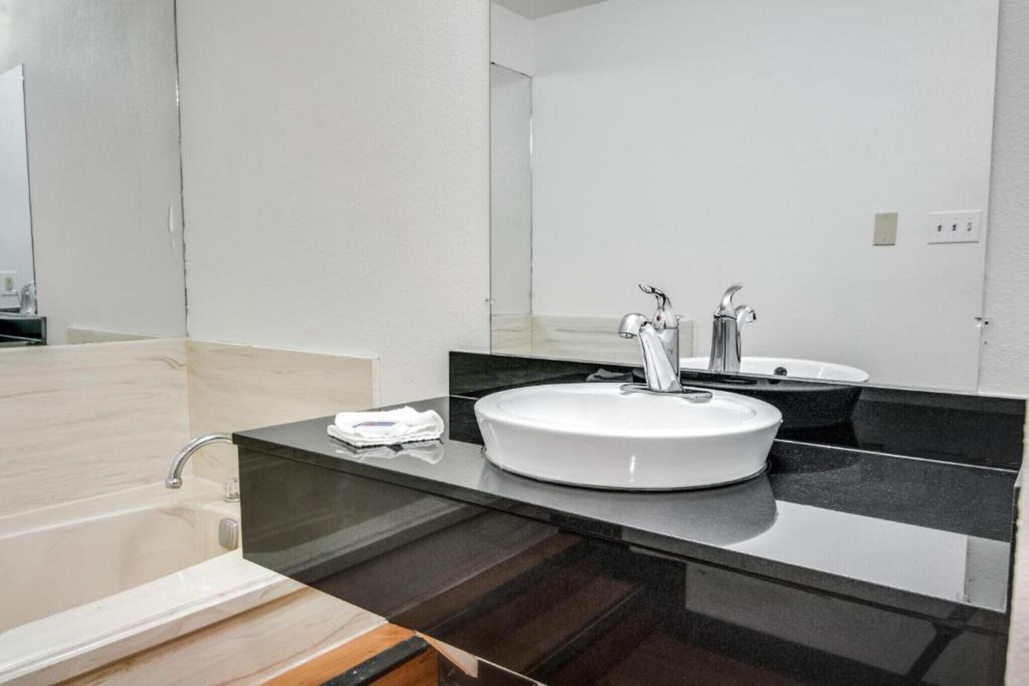 A modern bathroom with a round sink, a mirror, and a bathtub.