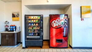 A vending machine area with a Pepsi machine and a Coca-Cola machine, a small cabinet with a cash register, and a sign on the wall.