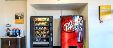 A vending machine area with a Pepsi machine and a Coca-Cola machine, a small cabinet with a cash register, and a sign on the wall.