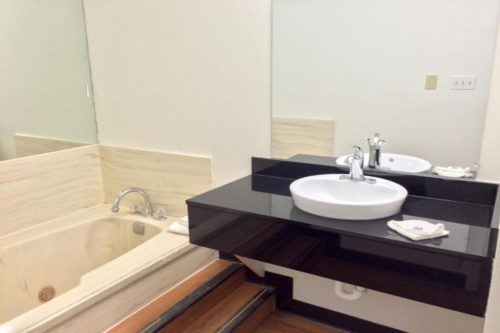 A bathroom with a bathtub, a white sink, a black countertop, and a mirror.