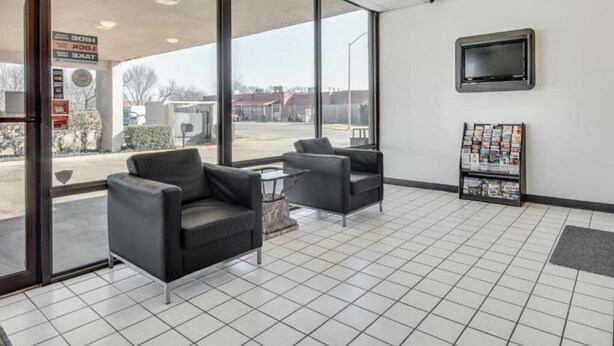 A hotel lobby with two armchairs, a coffee table, a TV mounted on the wall, and a magazine rack.
