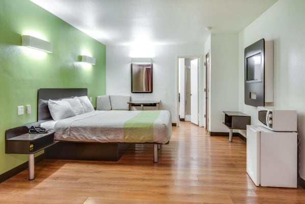 Una habitación de hotel con cama, mesita de noche, televisor y una pequeña kitchenette.