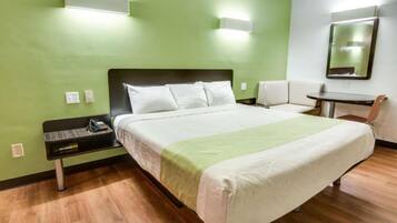 Ein Hotelzimmer mit einem großen Bett, einem Nachttisch, einem Sessel, einem kleinen Tisch und einem Spiegel an der Wand.