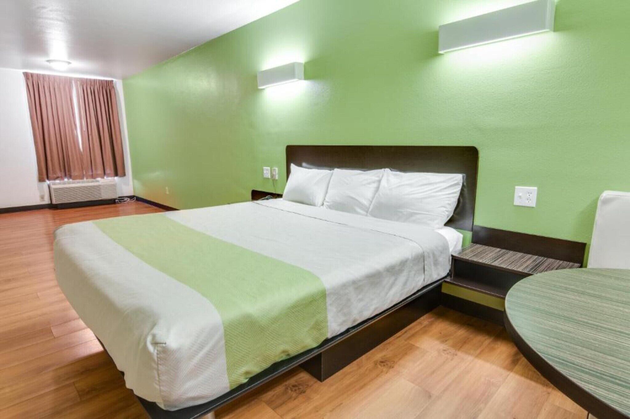 Una cama individual con una colcha verde y blanca, una mesita de noche, una silla y una lámpara fijada a la pared.