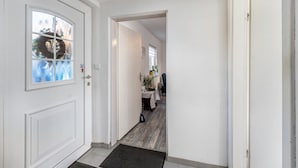 A hallway with a white door, a small table with a plant, and a coat rack. - Newly Built Holiday Apartment with Terrace (Klein Wittensee)