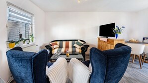 A living room with a sofa, two armchairs, a coffee table, a TV, and a dining area with a table and chairs. - Newly Built Holiday Apartment with Terrace (Klein Wittensee)