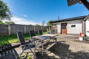 Um pátio com mesa e cadeiras, cerca de madeira e um pequeno edifício com porta e janela.