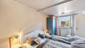 A bedroom with two beds, a bedside table with a lamp, a window with curtains, and a view of the outside. - Newly Built Holiday Apartment with Terrace (Klein Wittensee)