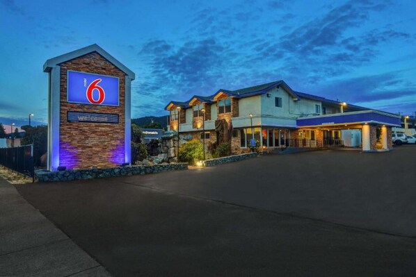 Un motel reconnaissable à son grand panneau en forme de « 6 », à sa façade en pierre et à son entrée bien éclairée.