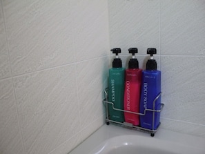 A bathroom with a white bathtub, a metal rack holding three bottles of shampoo, conditioner, and body soap.