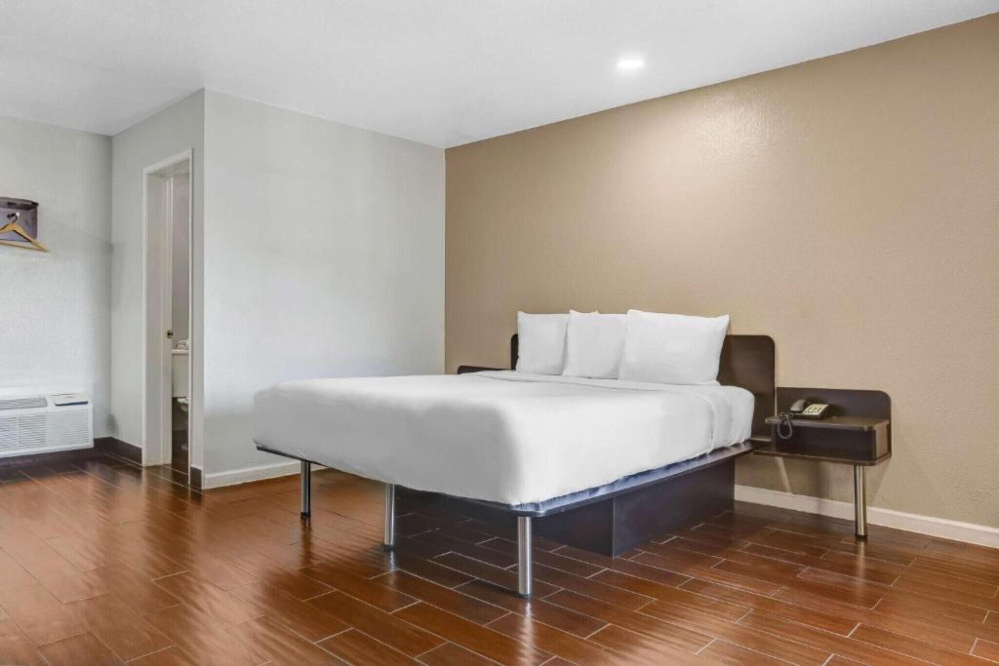 Une chambre d’hôtel avec un lit, une table de chevet avec un téléphone et une porte donnant sur une salle de bain.