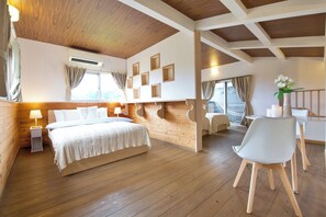 Ein Zimmer mit Holzboden, einem Bett mit weißer Bettdecke, einem Schreibtisch mit Stuhl und einem Fenster mit Vorhängen.