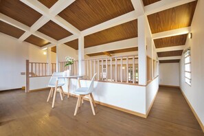 Ein geräumiges Zimmer mit hohen Decken, Holzbalken, einer weißen Geländer und einem Essbereich mit Tisch und Stühlen.