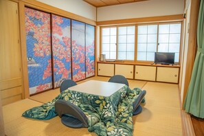 Una habitación japonesa tradicional con suelo de tatami, una mesa baja de tatami, televisor y puertas correderas shoji con motivos de cerezos.
