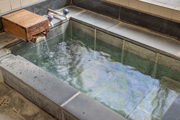 Un baño de aguas termales con un banco de madera, un grifo y una pared de azulejos.