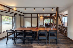 Een eetruimte met een houten tafel en stoelen, een trap en grote ramen.