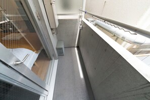 Ein schmaler Korridor mit Metallgeländer, einer kleinen Bank und einer Tür zu einem Zimmer mit Fenster.