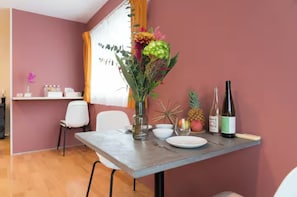 Ein Essbereich mit einem Tisch, der für zwei Personen gedeckt ist, einer Vase mit Blumen, einer Weinflasche und einer Ananas auf dem Tisch.