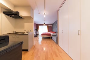 Ein kleines Hotelzimmer mit Küchenzeile, einem Bett mit roter Bettwäsche, einem Schreibtisch mit Stuhl und einem Kleiderschrank.