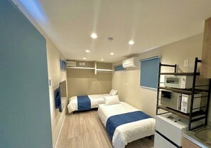Habitació d'hotel senzilla amb dos llits, petita cuina i aire condicionat integrat.