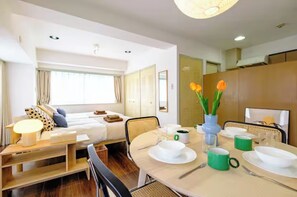 Ein Hotelzimmer mit Bett, Nachttisch, Lampe, Esstisch gedeckt mit Tellern, Tassen und einer Vase mit Blumen.