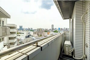 Ein Balkon mit Blick auf die Stadt, einem Metallgeländer und einer weißen Wand mit Lüftung.