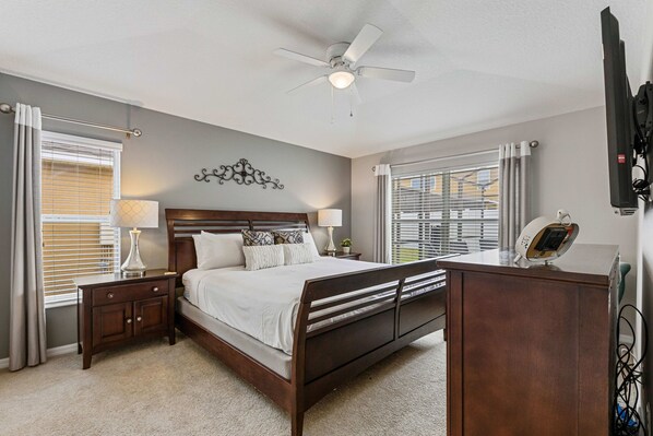 A bedroom with a bed, bedside tables, a ceiling fan, a TV, and a window with blinds. - 2541 Dharma Circle (Kissimmee)