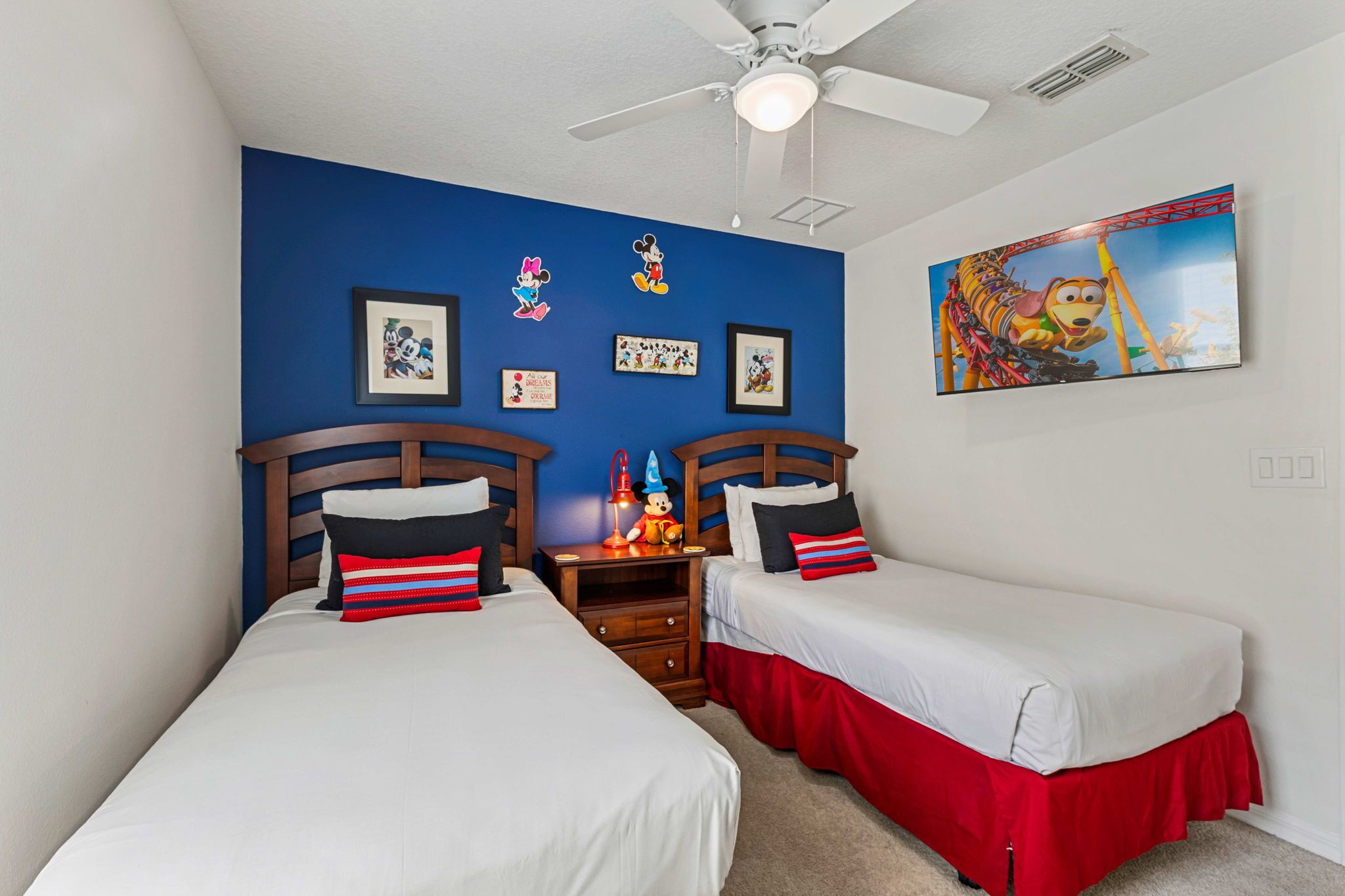 A bedroom with two beds, a ceiling fan, and wall decorations including framed pictures and a large painting.