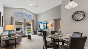 A modern living room with a dining area, a large window, and a clock on the wall. - 2541 Dharma Circle (Kissimmee)