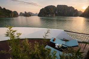 A serene outdoor seating area with a view of a calm body of water and distant mountains. - Amour Cruise (Tuan Chau)