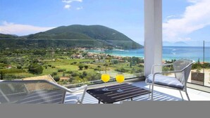A balcony with a table and chairs, overlooking a coastal landscape with mountains and a town. - Omicron & White Villas (Lefkada)