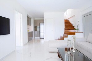 A modern living room with a glass coffee table, a white sofa, and a staircase leading to another level. - Omicron & White Villas (Lefkada)