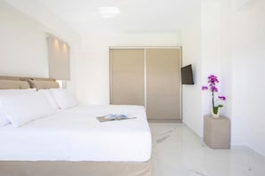 A hotel room with a bed, a wardrobe, a flat-screen TV, and a potted orchid. - Omicron & White Villas (Lefkada)