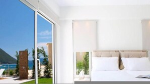 A modern hotel room with a large bed, a view of the ocean, and a sliding glass door leading to a balcony. - Omicron & White Villas (Lefkada)
