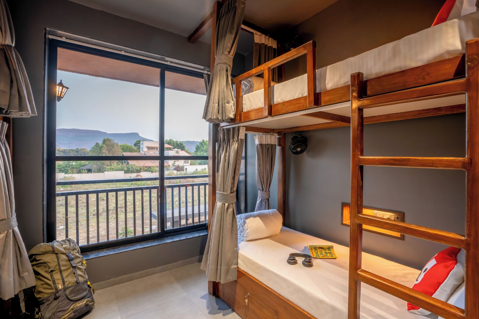 A room with bunk beds, a window with a view, a fan, and a small table with headphones.