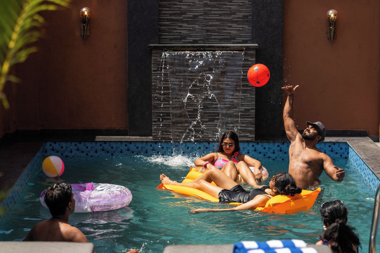 Una piscina con gente sobre flotadores, un elemento acuático y una pared de azulejos.