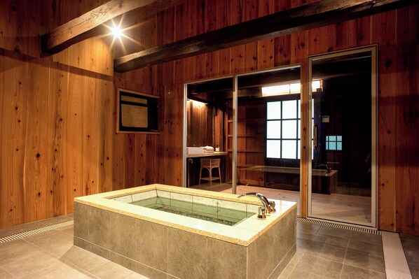 A wooden interior with a large bathtub, a chair, and a sliding glass door leading to another room.