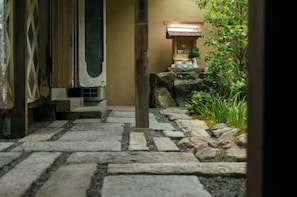 Un sentier de pierres mène à une construction traditionnelle japonaise, dotée d’un toit en bois et d’un petit sanctuaire.
