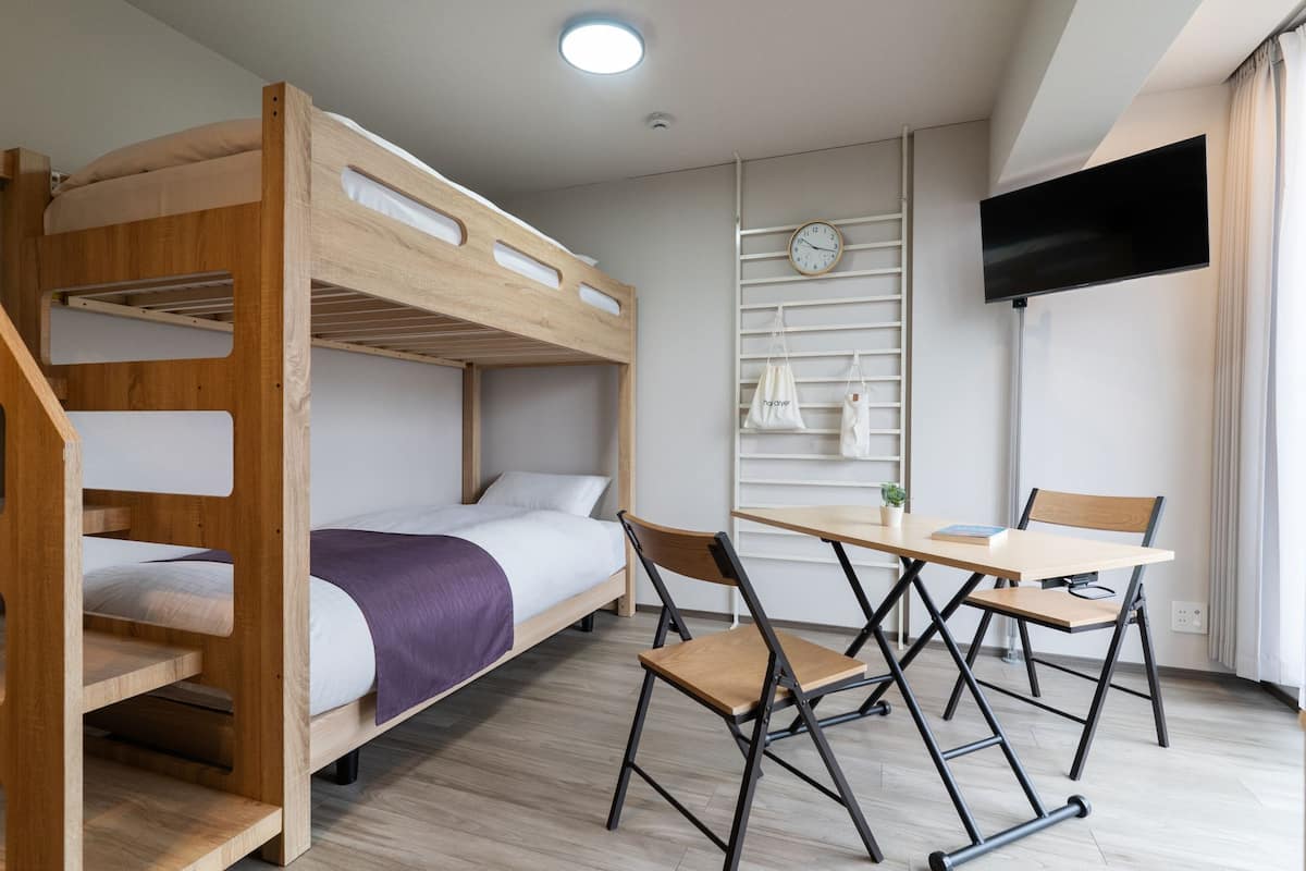 A bunk bed room with a desk, chair, and a TV mounted on the wall.