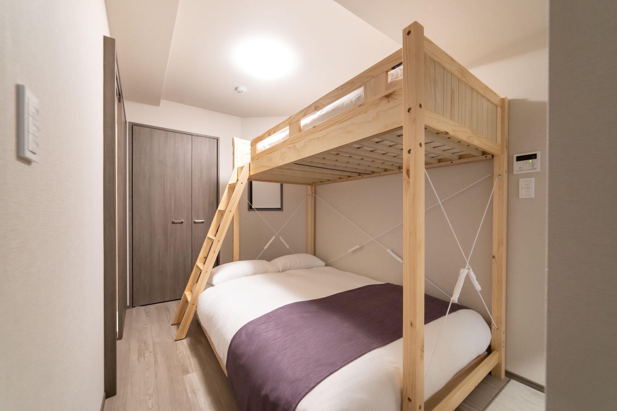 Uma cama beliche com escada, porta e interruptor de luz na parede.