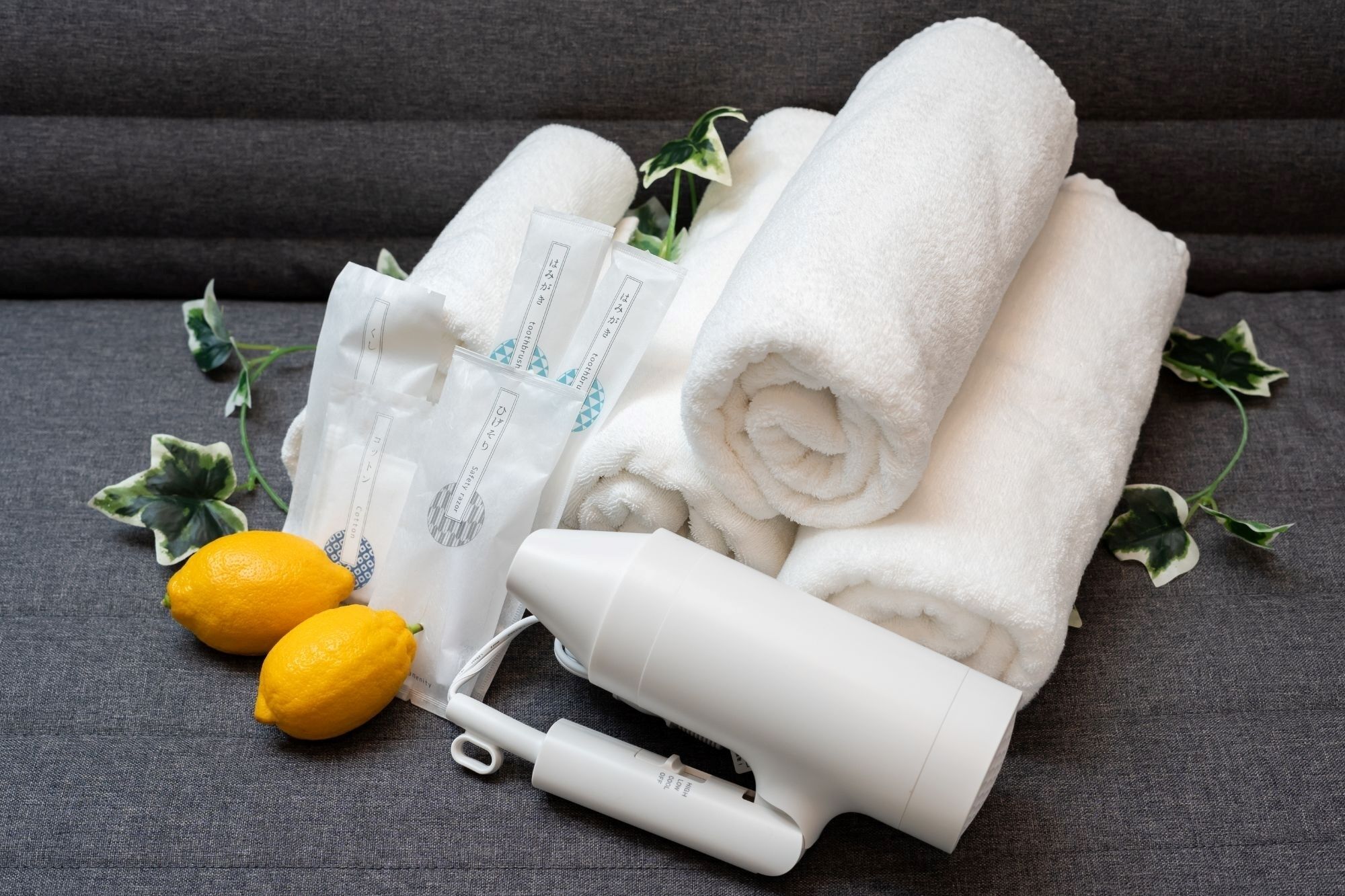 A set of white towels, a white portable heater, and two lemons on a grey fabric surface.