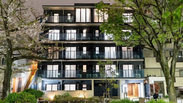 Un edificio de varios pisos con balcones, grandes ventanales y un jardín cuidado.