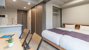 Una habitación de hotel con cama, escritorio, silla, planta pequeña y microondas.