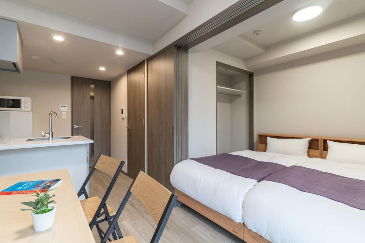 A hotel room with a bed, a desk, a chair, a small plant, and a microwave.