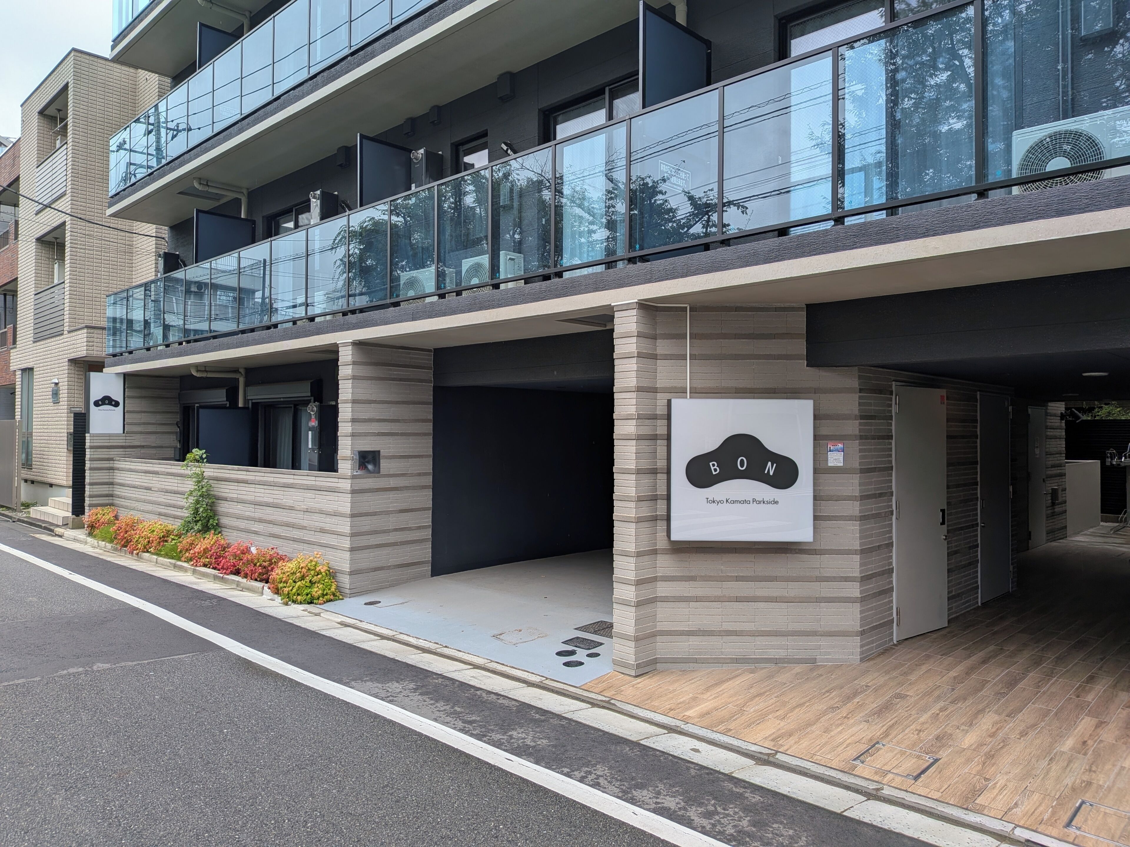 A modern building with a glass balcony, a sign indicating 'Tokyo Kamato Parkside,' and a brick facade.