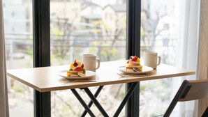 Una mesa con dos platos de postre y dos tazas, frente a una ventana con vistas a edificios.