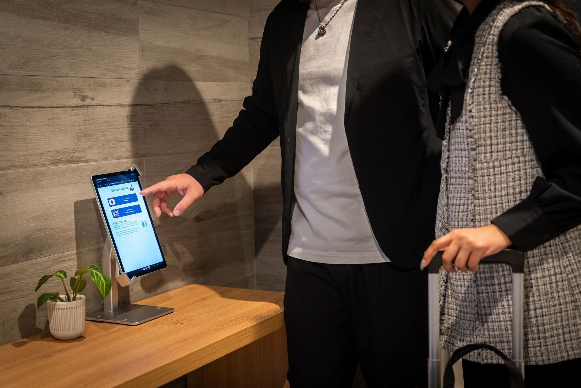 Una persona interactúa con un quiosco digital en un entorno moderno con un banco de madera y una planta en maceta.